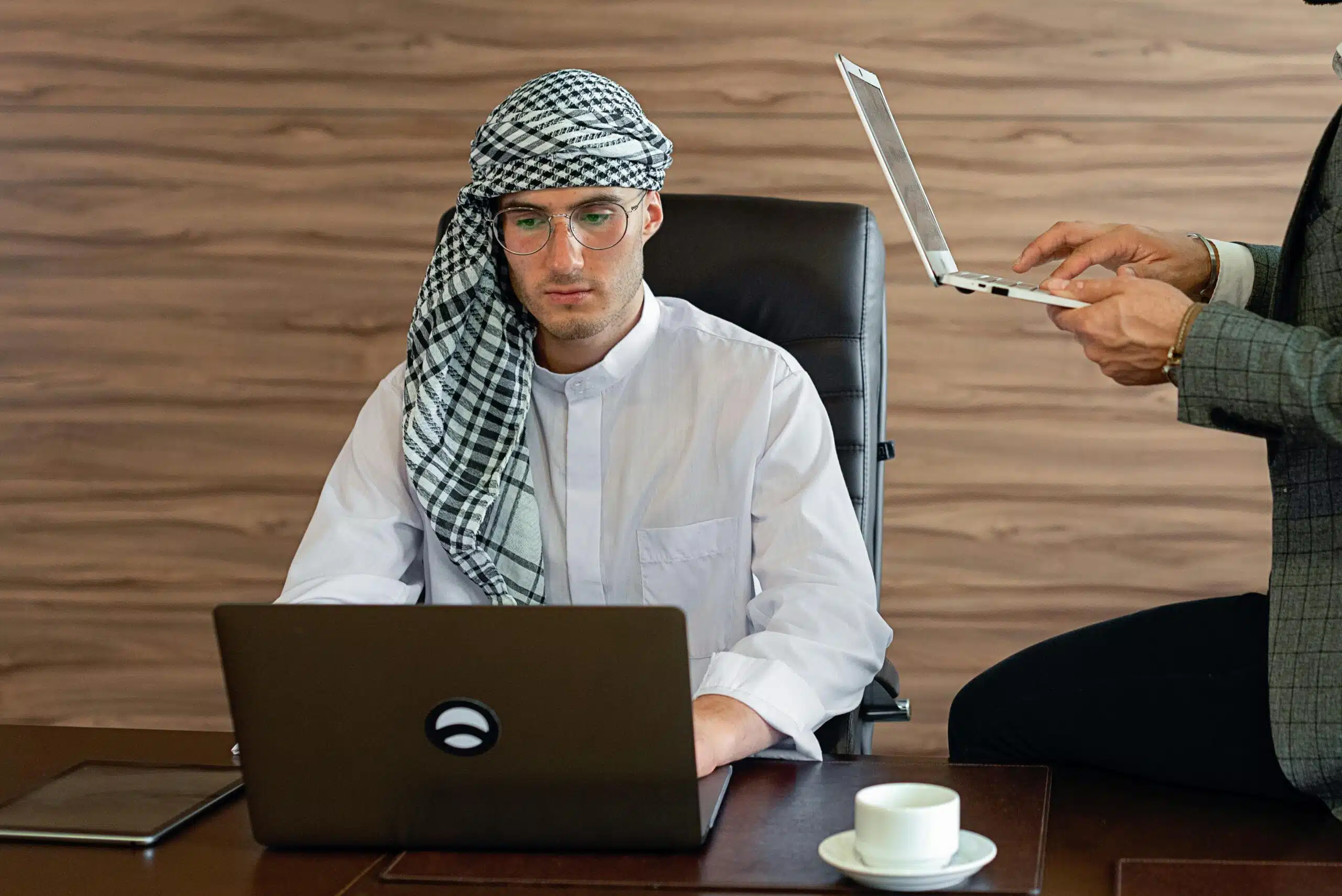 Middle Eastern businessman in office attire focused on work with laptops.